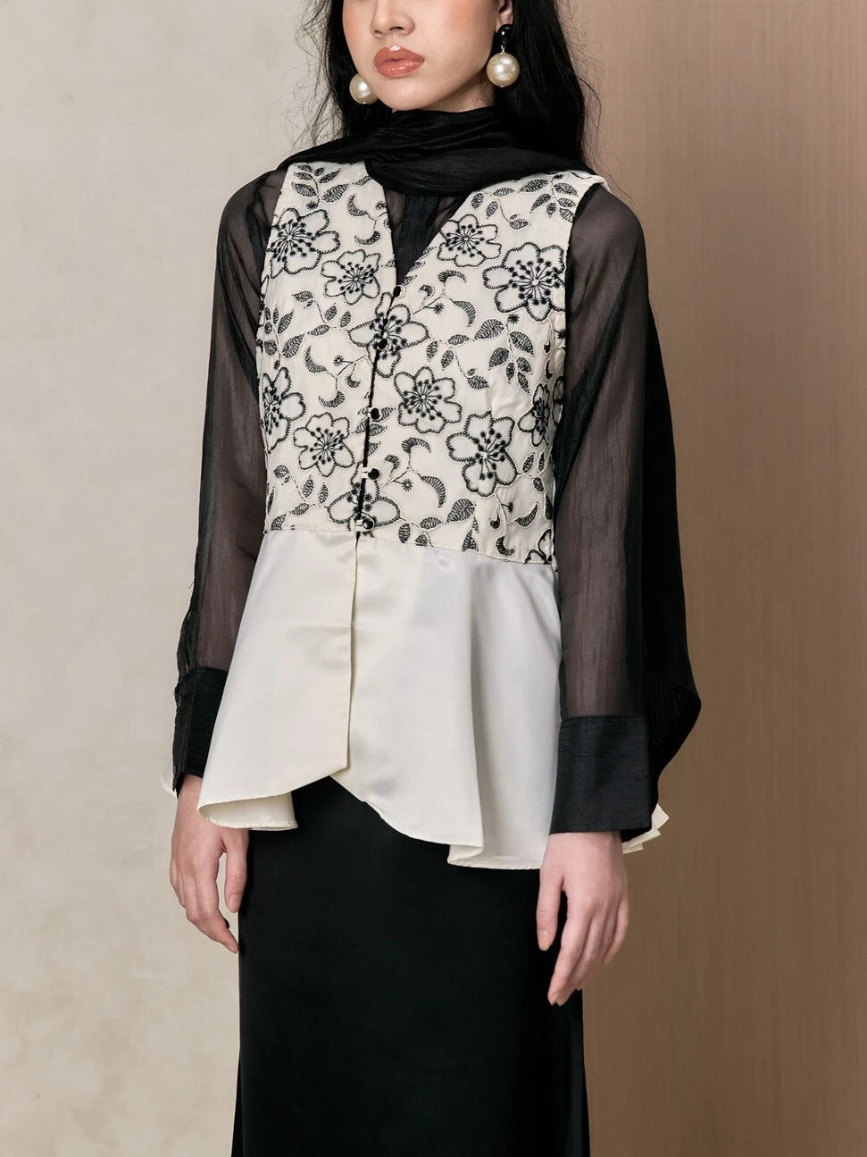 Woman wearing a layered outfit with a floral vest and black sheer sleeves by Studio Tui on a beige background