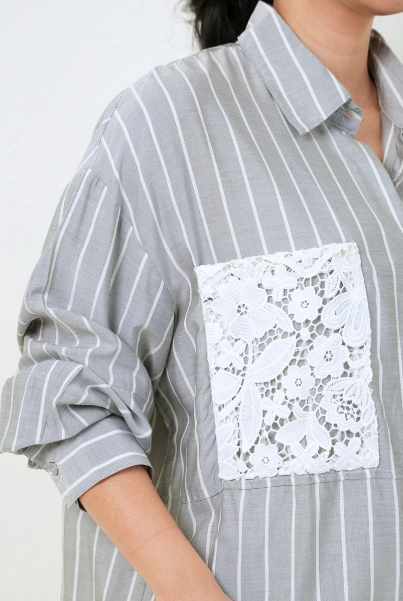 A close-up of a gray and white vertically striped button-up shirt by Studio Tui with a large white floral lace pocket on the chest, worn by a model.