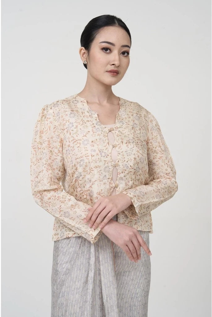 A woman wearing a beige batik long-sleeved outer top by Kartinis Label with front buttons and a matching skirt, standing against a neutral background.
