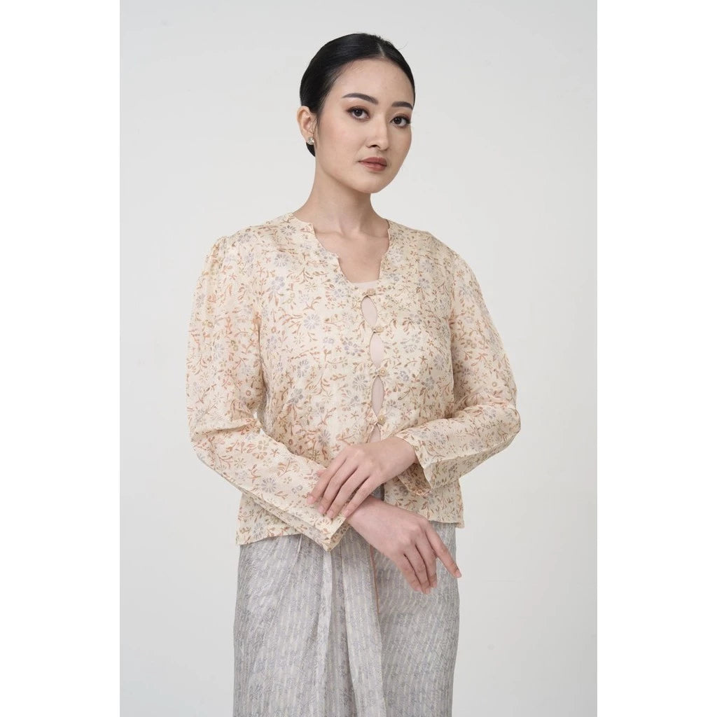 A woman wearing a beige batik long-sleeved outer top by Kartinis Label with front buttons and a matching skirt, standing against a neutral background.