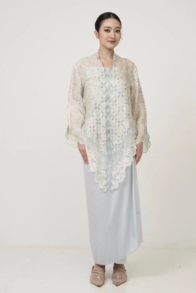 A woman wearing an ivory Kebaya by Kartinis Label with long bell sleeves and front button design, standing against a white background.