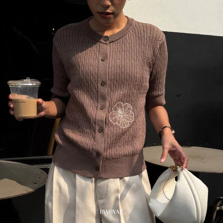 A woman wearing a mocca colored short-sleeve cable knit cardigan with a floral embroidery on the front from BWBYAZ, paired with a white skirt.