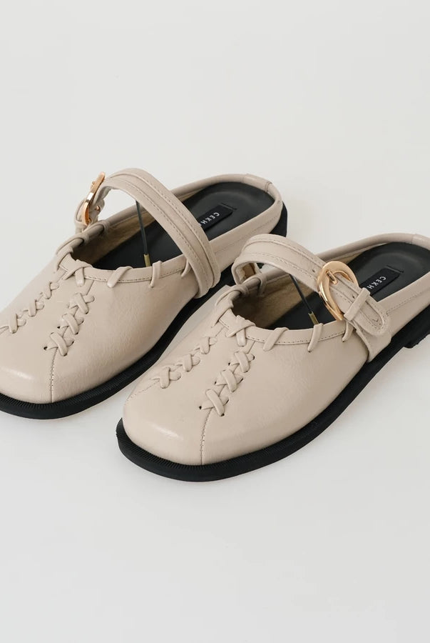 Pair of beige mules sandals by Cekhas with black soles on a light gray background