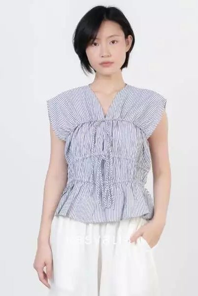 A model wearing a grey and white vertically striped peplum top by Kasyalia with ruffled details and white wide-leg pants, set against a plain light gray background.
