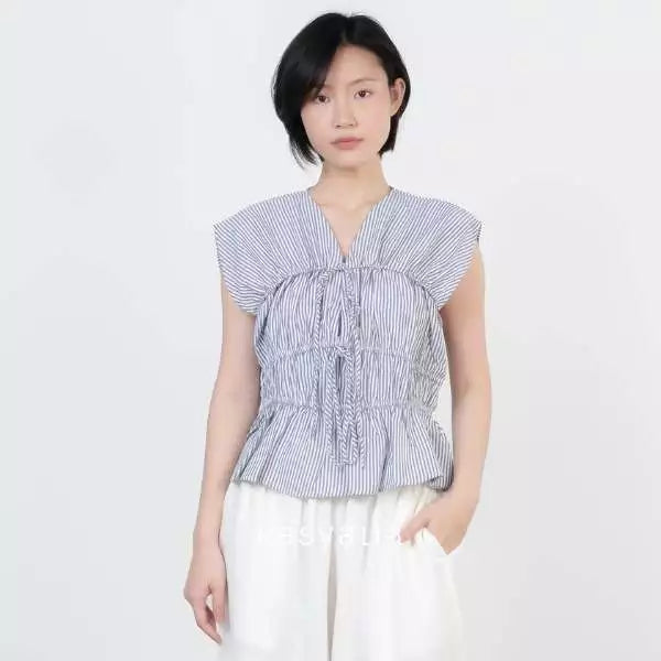 A model wearing a grey and white vertically striped peplum top by Kasyalia with ruffled details and white wide-leg pants, set against a plain light gray background.