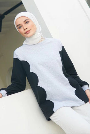 Woman wearing a white and black patterned sweater by Casa Elana with a hijab, sitting on a white surface.