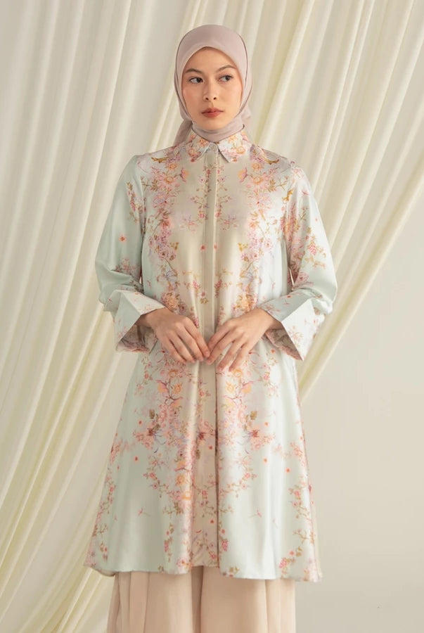 Woman wearing a light-colored floral tunic by Hijabchic with a hijab against a white curtain background.
Seorang wanita mengenakan tunik bermotif bunga berwarna terang dari Hijabchic dengan hijab di depan latar belakang tirai putih.
