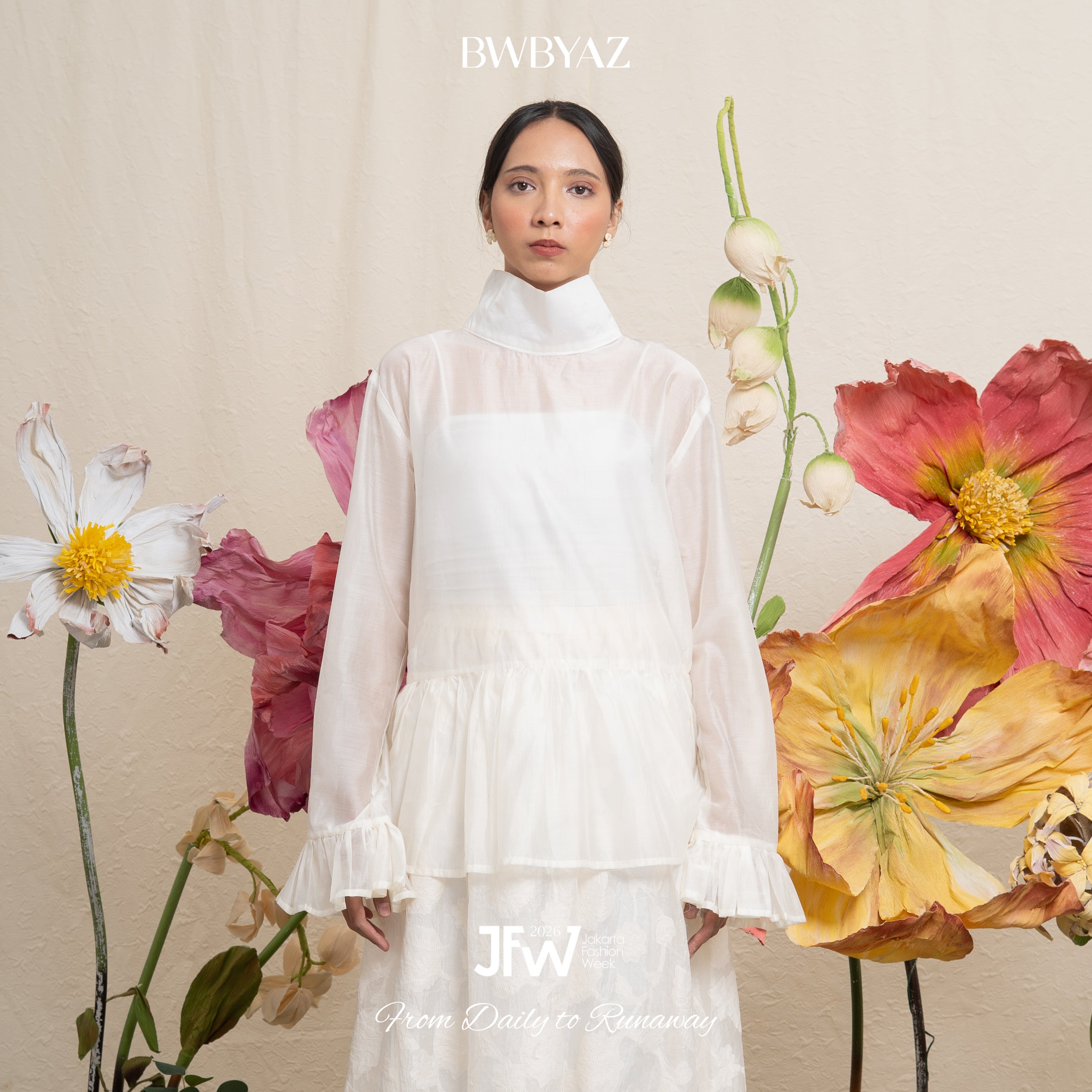 Woman in a white ruffle blouse standing among flowers with 'BWBYAZ' branding.