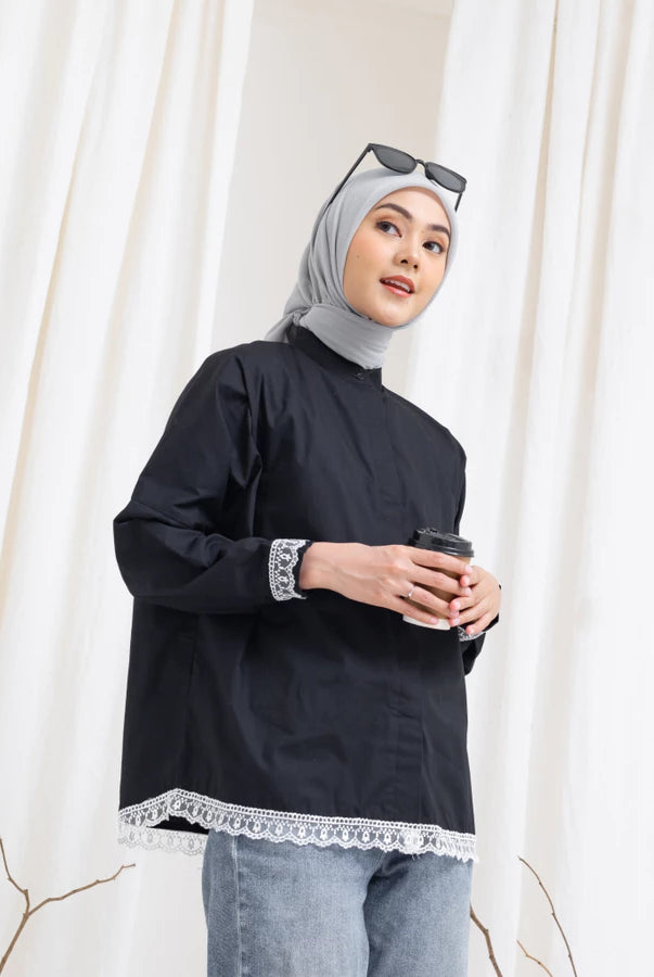 Woman wearing a black shirt by Abame with lace trim and gray hijab, holding a coffee cup against a white curtain background.