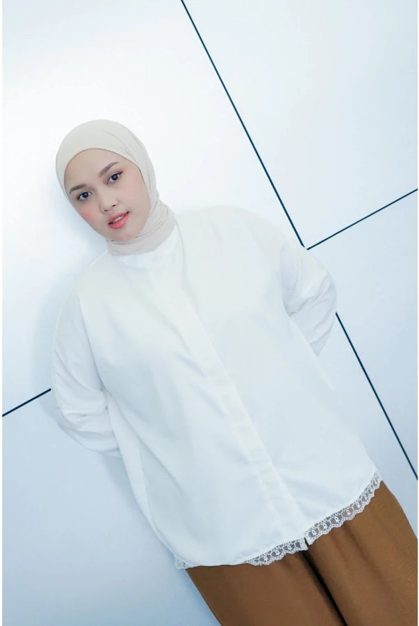 Woman wearing a white hijab and white shirt by Abame with brown pants on a light blue background