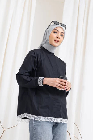 A woman wearing a black Chiky Shirt by Abame with white lace details, holding a cup, with a grey hijab and sunglasses on her head.