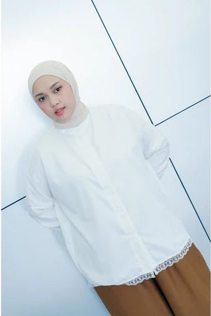 Person wearing a white long-sleeve shirt by Abame with lace trim on a light blue background