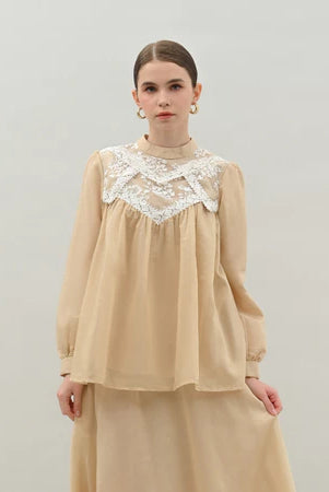 Woman wearing a light beige blouse by Kasa Heritage with lace details on a plain background
