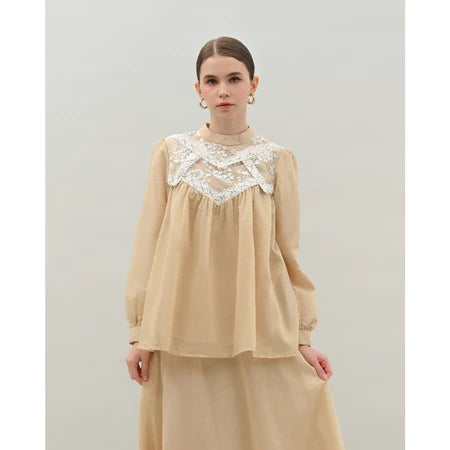 Woman wearing a light beige blouse by Kasa Heritage with lace details on a plain background