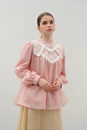 Woman wearing a pink blouse by Kasa Heritage with lace details on a plain background