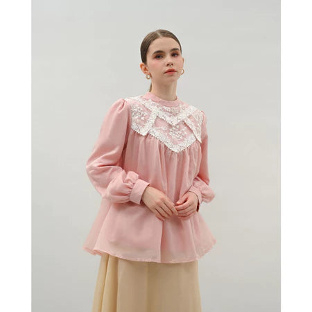 Woman wearing a pink blouse by Kasa Heritage with lace details on a plain background