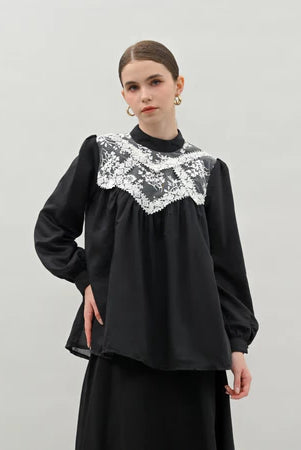 Woman wearing a black blouse by Kasa Heritage with lace detailing on a light gray background