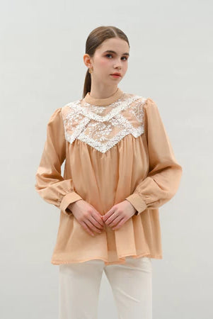 Woman wearing a beige blouse by Kasa Heritage with lace details on a plain background