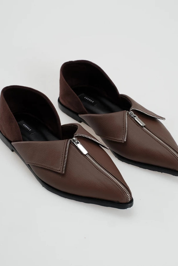 A pair of dark brown leather pointed-toe flat shoes with silver-tone zipper details across the vamp by Cekhas, displayed on a light gray background.