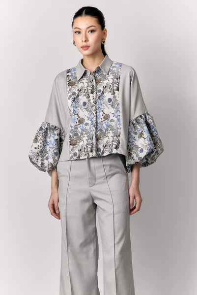 Woman wearing a gray outer by Studio Tui with floral cuffs and a matching skirt on a light gray background