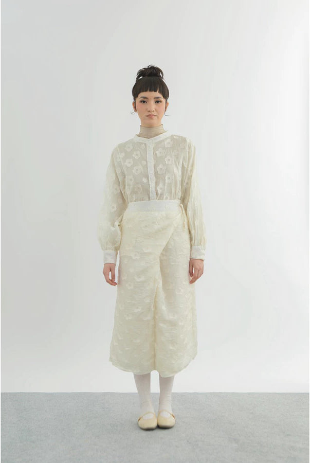 Person wearing a long, light-colored top and wrap skirt by Yestoday with a sheer overlay against a white background
