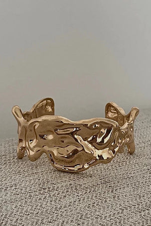 Gold bracelet by Darje on a textured surface with a neutral background