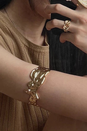 Close-up of a person wearing a gold bracelet and ring by Darje on a neutral background