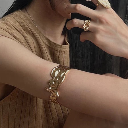 Close-up of a person wearing a gold bracelet and ring by Darje on a neutral background