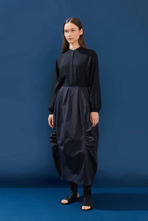 Woman wearing a black top and black pleated skirt by Yestoday against a blue background