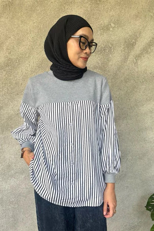 Woman wearing a gray and black striped shirt by Casa Elana with a hijab against a textured wall.