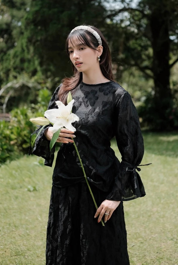Woman in a black floral blouse by Renaette holding a white flower in a garden setting