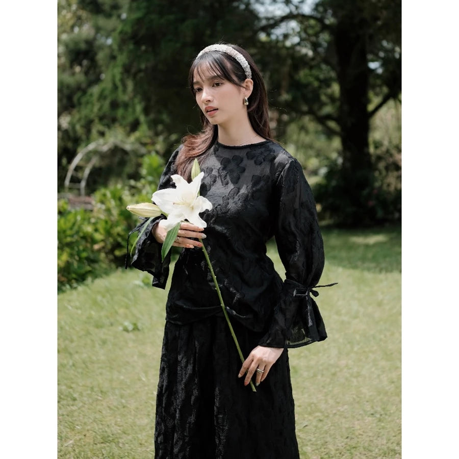 Woman in a black floral blouse by Renaette holding a white flower in a garden setting