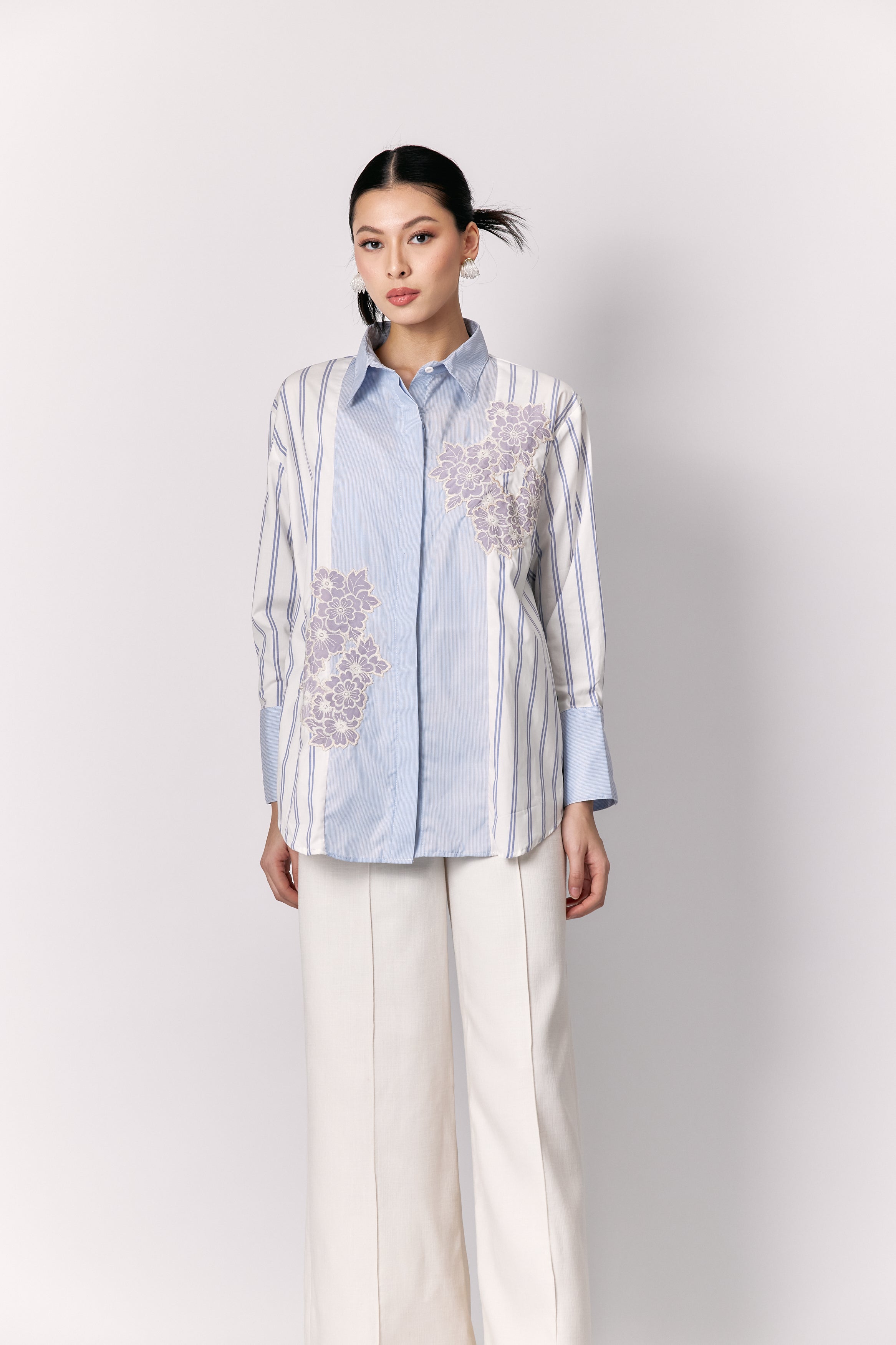 Woman wearing a light blue and white striped shirt with floral embroidery by Studio Tui on a white background