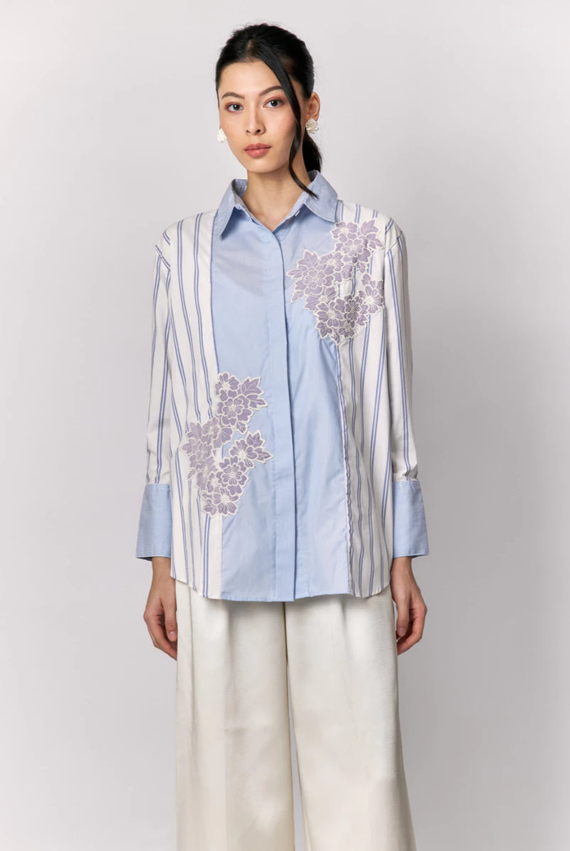 Woman wearing a light blue shirt by Studio Tui with floral embroidery on a plain background