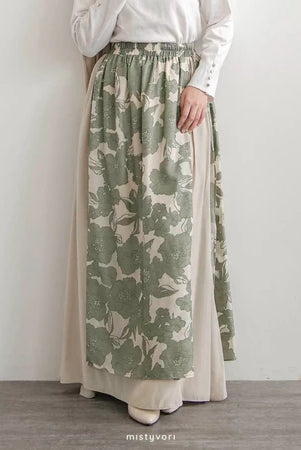 Person wearing a long green and beige patterned skirt by Mistyvori with a plain white top against a light gray background.
