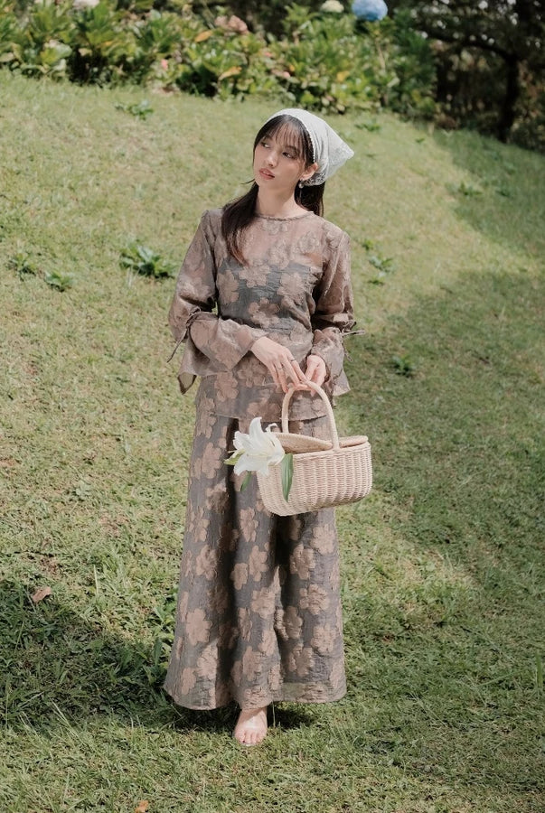 Woman in a ash brown floral outfit with floral embroidery by Renaette holding a basket in a grassy field
