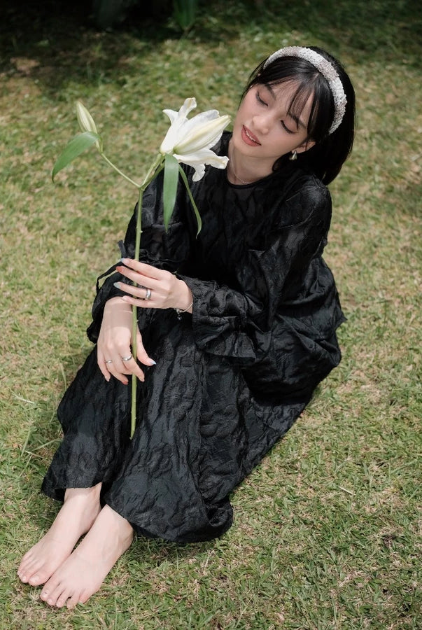 Person in a black outfit with floral embroidery by Renaette holding a white flower on grass