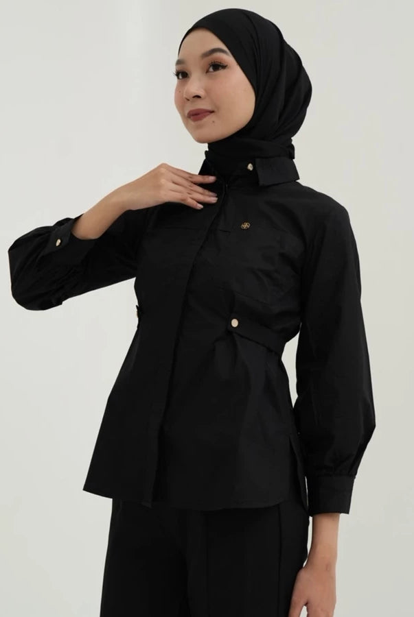 Woman wearing a black blouse by Tunique with a matching hijab against a plain background