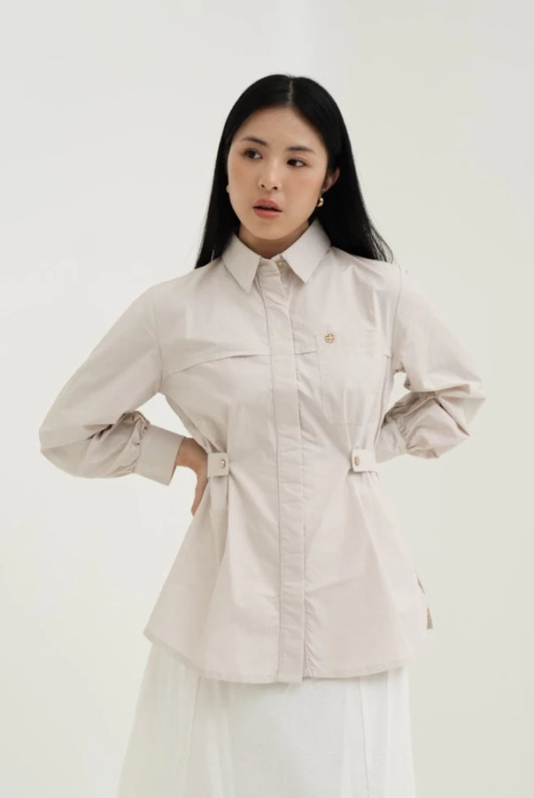 Woman wearing a light-colored blouse by Tunique with a belt against a white background