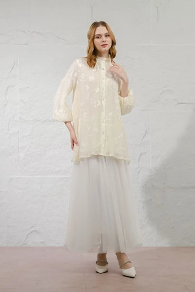 Woman wearing a ivory-colored Della Blouse by Kasa Heritage with a textured top and sheer skirt against a white background