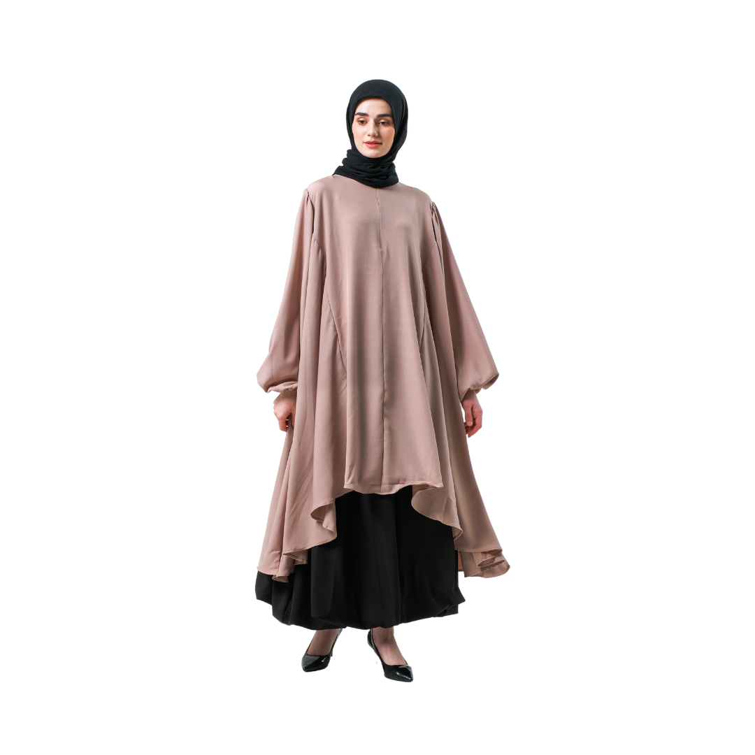 A woman wearing a blush pink tunic with a round neckline and long sleeves, paired with a black skirt and a black headscarf.