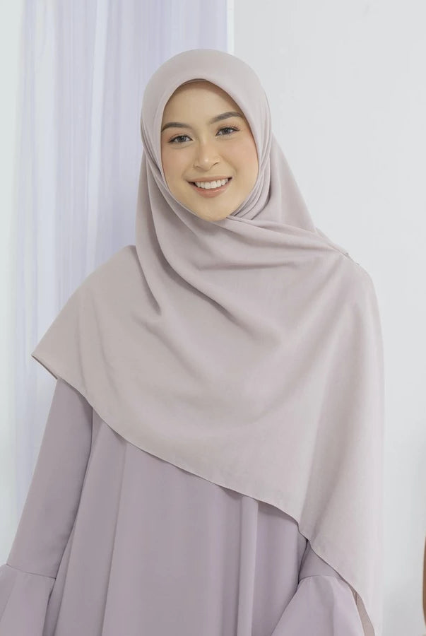 Woman wearing a beige square hijab by Lozy Hijab and dress against a white curtain background