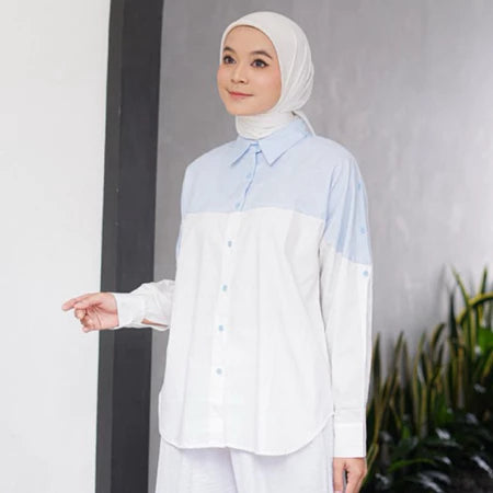 Woman wearing a light blue and white shirt by Casa Elana with a hijab against a gray wall.