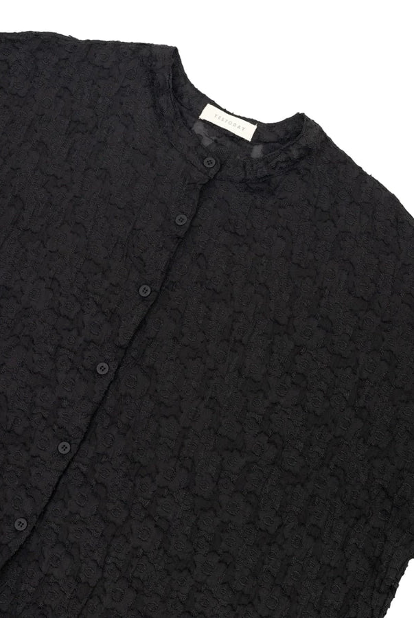 A close-up of a black textured button-up shirt by Yestoday with a stand collar, laid flat against a white background.