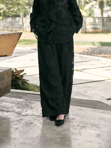 Person wearing a black lace pants by Studio Tui standing on a concrete surface with blurred background