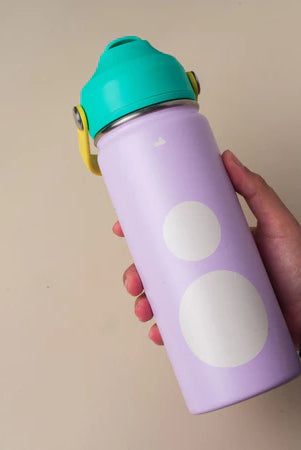 Purple water bottle with white polka dots and a green lid from Muhajir Project held by a hand against a beige background