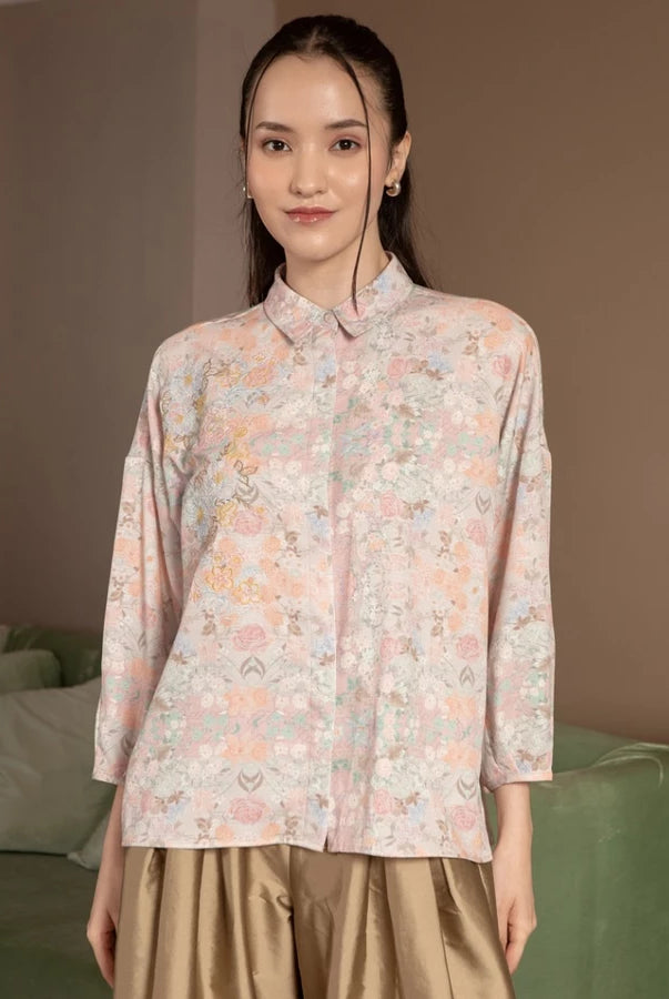 Woman wearing a floral blush shirt by Hijabchic standing in a room with a couch.