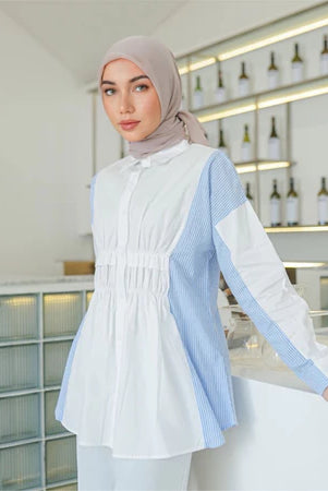 Woman wearing a white and blue striped shirt by Casa Elana with a hijab in an indoor setting.