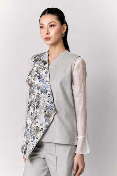 Woman wearing a floral vest by Studio Tui over a light shirt with gray pants on a white background