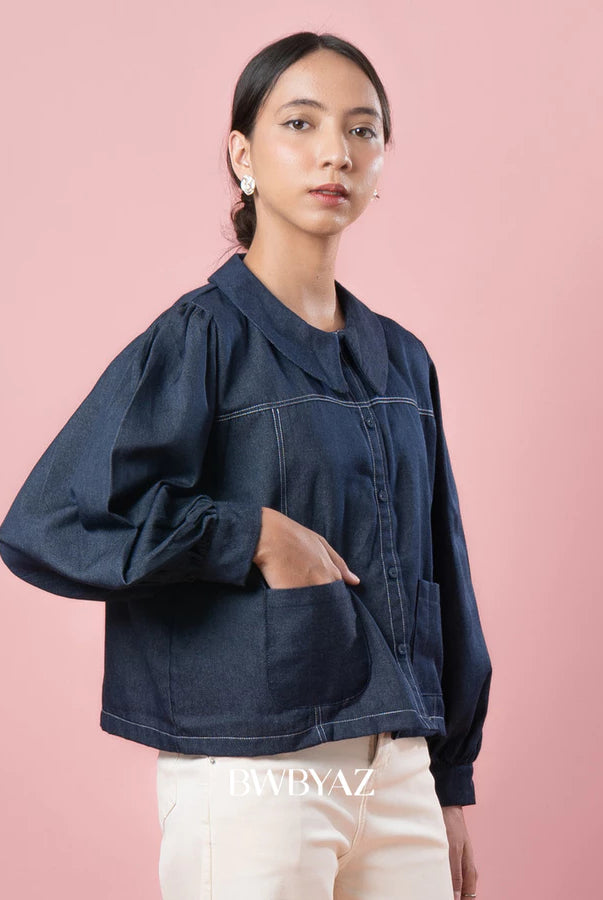 Woman wearing a indigo blue denim jacket against a pink background with 'BWBYAZ' branding.